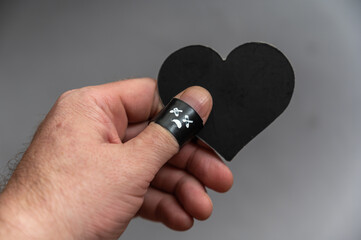 Middle-aged man holds black heart in his hand. Phalanx of his thumb is wrapped in black electrical...