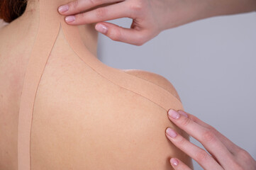 Fototapeta premium Female doctor glues kinesio tapes on the patient's shoulder. 