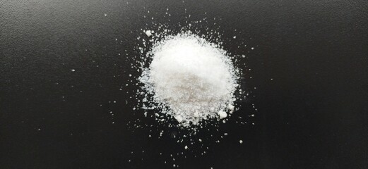 Pile of pure white cocaine or heroin powder isolated and scattered on black table background with...