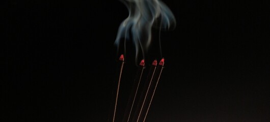 Aromatic agarbathi, agarbatti or Incense sticks smoldering in room with smoke and aroma. Isolated in dark black background with copy space. It used in asian religious prayer. Closeup macro side view.