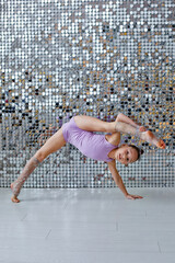 A gymnast girl in a purple suit performs stretching exercises and acrobatic exercises on a silver...