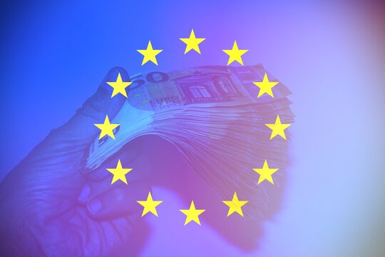 Hand holding European banknotes with the European Flag as background.