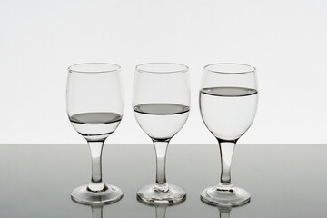 Three wine glasses filled with water reflected on the table