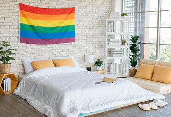 Large rainbow colorful gay pride flag hanging on brick wall pattern background over bed in modern...