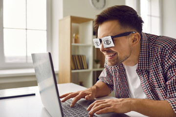 Funny weird sleepy man with sticker eyes glued to eyeglasses working on modern laptop. Tired...