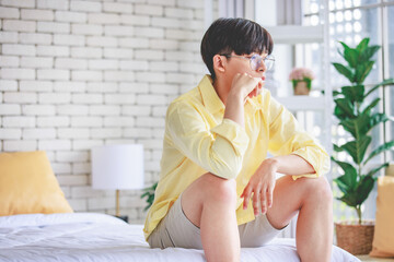 Closeup shot of Asian young upset unhappy thoughtful teenager gay man boyfriend sitting alone on bed having problem trouble and serious thinking after conflict argument fighting with lover couple