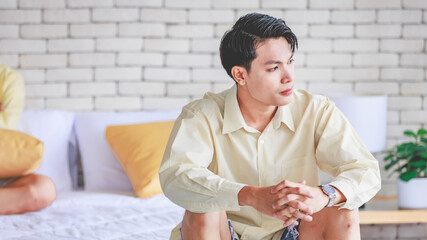 Closeup shot Asian young upset unhappy thoughtful teenager gay man boyfriend sitting alone on bed crossed arms holding pillow leaning on brick wall thinking after having argument fighting with lover
