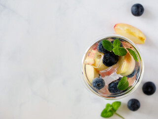 Blueberry and peach infused water, cocktail, lemonade or tea in double glass. Summer iced cold drink with blueberry, ice, peach and mint on grey marble background, copy space, top view flat lay