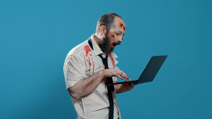 Dirty spooky zombie with open bloody wounds and scars using modern laptop. Dumb acting brain-eating...