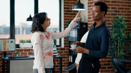 Brain dead zombie woman touching businessman while discussing. Doomsday survivor talking with dangerous dead walking corpse having bloody and deep wounds in office workspace.