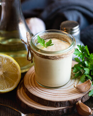 Aioli sauce in a glass jar on a wooden background, selective focus