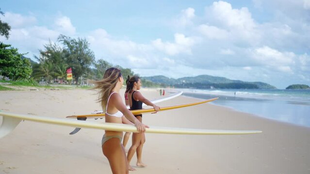 4K Group of Asian woman surfer in swimwear holding surfboard walking together on tropical beach in sunny day. Female friends enjoy outdoor activity lifestyle water sport surfing on summer vacation