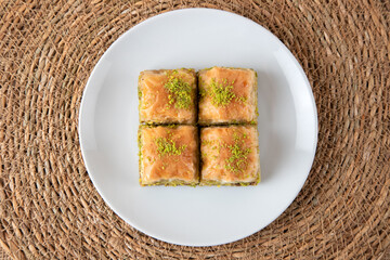 Pistachio baklava on a white plate. A plate of baklava on a wicker background