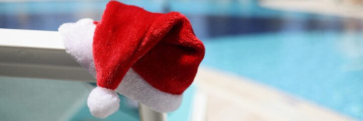 Santa claus hat put on lawn chair near swimming pool with clean turquoise water