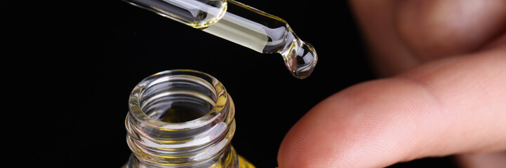 Person dripping drop of extract oil on finger with eyedropper
