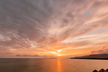 Gorgeous sunrise on horizon, colorful clouds in motion blur, sun reflected on sea surface.