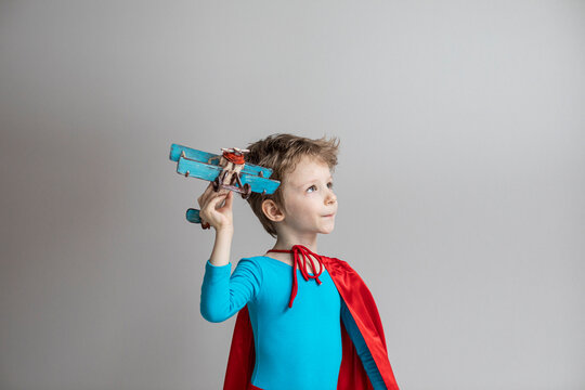 Boy dressed as a super hero in a red cape plays with an airplane at home. Travel.