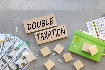 DOUBLE TAXATION . two wooden blocks with text on a gray background. green notepad calendar