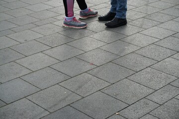 Liebespaar mit zwei Schuhpaaren und Hosenbeinen auf nassem grauem Steinplattenbodenplatz in Stadt  bei Regen am Abend 
