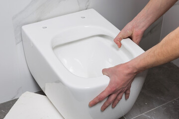 hands of the master hold a new toilet bowl, try on against the wall before installation