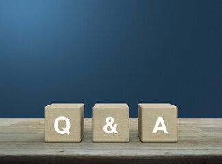 Q and A letter on wood block cubes on wooden table over light blue wall, Business customer service...