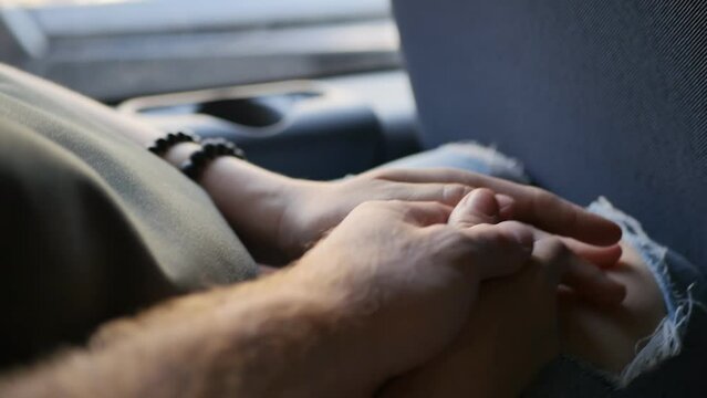 a man's hand touches and squeezes a woman's hand while sitting next door in the passenger seat of the bus by the window while moving on the way. Love and affection in a relationship.