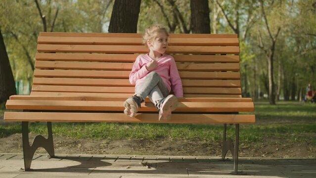Little girl suffers from hot weather sitting on bench in park. Blonde child rests in city garden on hot spring day. Smothering heat in city