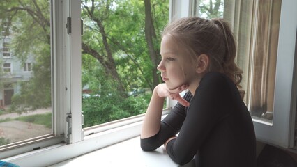 A girl of nine looks out the window from her house.