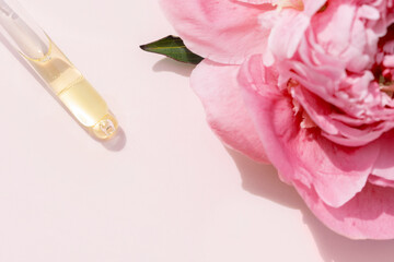 pipette with face serum with a peony flower on a pastel pink backround