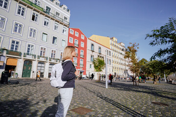 Traveling by Portugal. Happy young woman with rucksack walking by street in Lisbon.