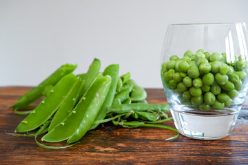 Green peas in glass bowl. fresh pea in the pod with green leaves. green peas on a brown wodden table
