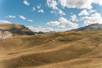 mountainous landscape of dry grass with a road and the blue sky with some clouds in the background