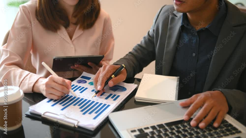 Poster business documents on office table with smart phone and laptop and two colleagues discussing data in