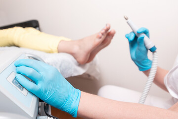 A pedicurist turns on the foot peeling machine. Defocused client's legs are in the background. The...