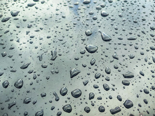 Water drops on light car surface covered in wax with cloudy sky reflection on light grey paint