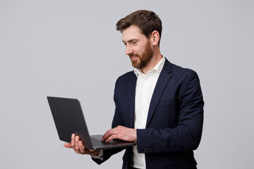 Handsome man in suit working online on laptop over grey studio background