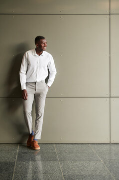 Full body of content African male entrepreneur in formal clothes looking into distance while standing near wall of building