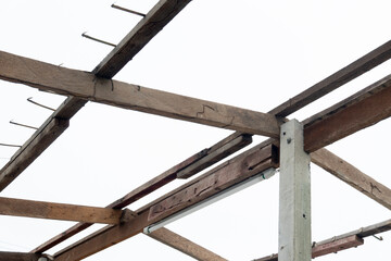 Demolition of wooden roof structures. There are cement poles and steel attached to the roof attached to the wooden frame. Under the white sky.