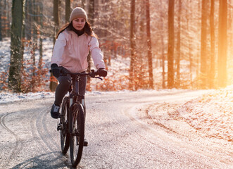 Obraz premium A woman rides a bike in winter. Concept of cycling during snowy weather. Snow and sun weather in the park