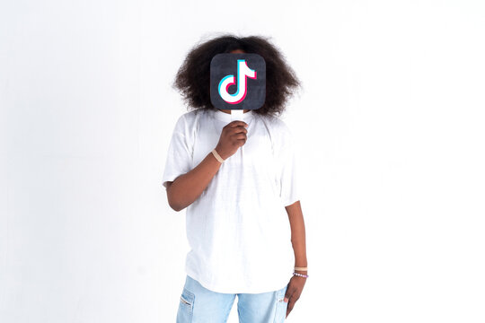 African american teenager holding a  Tiktok logo picture in his hands on a white background. Teenagers addicted to new technology trends - concept of youth, technology, social and friendship. 