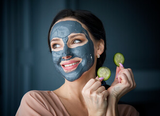 beautiful young woman with grey mask on face and cucumber slices