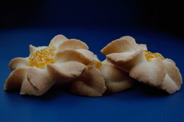 Three shortbread cookies in close - up on a blue background . Kurabye cookies with jam . Beautiful cookies in the shape of a flower side view.