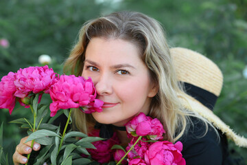 Fototapeta premium Beautiful young woman with a bouquet of bright pink peonies near her face, close-up. Summer vacation and travel concept