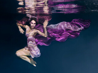 woman in colorful clothes on the dark background swimming underwater