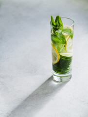 infused cucumber water in long glass.  summer drink with lemon and mint on light gray  concrete background. copy space