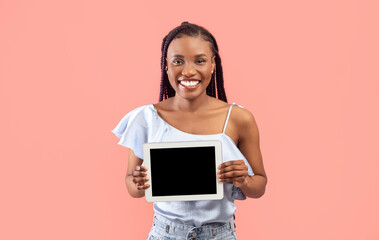 Pretty young black woman holding tablet with empty screen on pink studio background, mockup