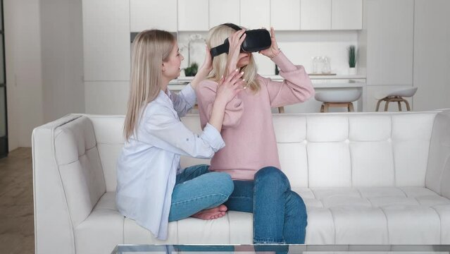 Adult daughter showing to her older mother using new technology to exploring the virtual world while sitting in the sofa, senior w, sitting on sofa at home.