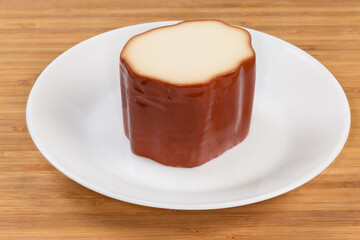 Piece of smoked processed cheese on dish on wooden surface