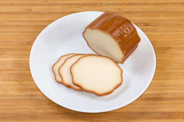 Partly sliced smoked processed cheese on dish on wooden surface