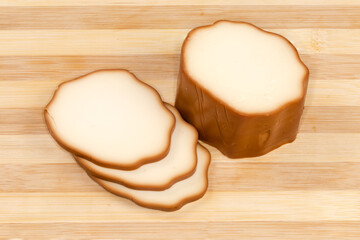 Partly sliced smoked processed cheese on a wooden cutting board